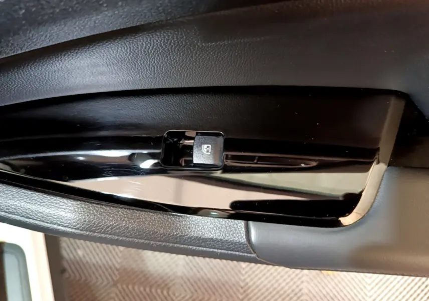 Bouton de commande de lève-vitre électrique noir sur panneau de porte intérieur du Kia Sportage blanc, vue rapprochée.