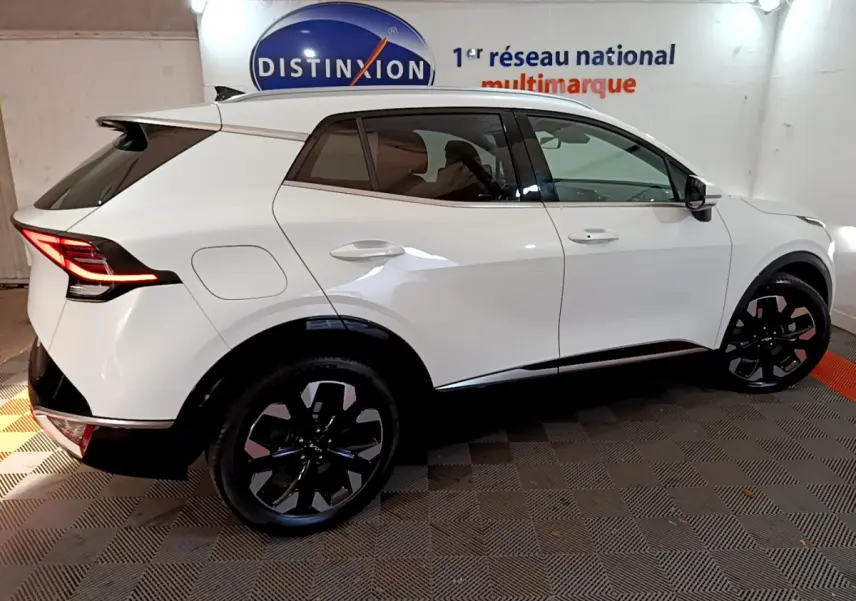 KIA SPORTAGE blanc en vue profil côté gauche, avec jantes noires et feux arrière LED allumés dans un showroom.