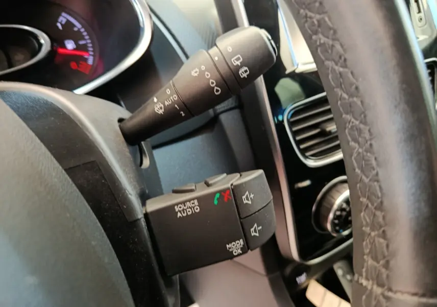 Gros plan sur la commande audio au volant et la manette d’essuie-glace d’une Renault Clio Intens rouge, intérieur noir.