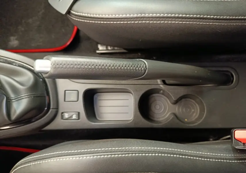 Vue plongeante sur la console centrale noire de la Renault Clio Intens avec frein à main manuel et porte-gobelets.