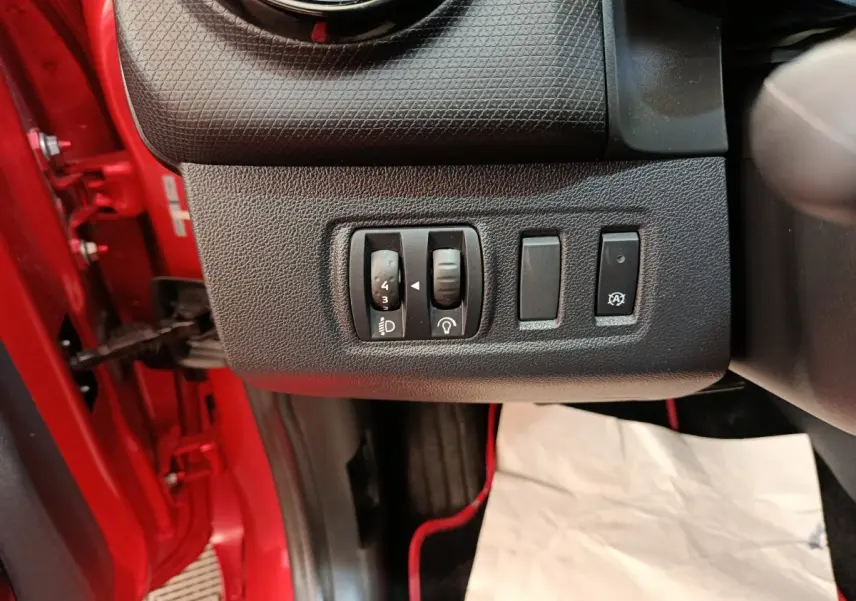 Vue intérieure côté conducteur de la Renault Clio Intens rouge, avec commandes de réglage des phares et fonction arrêt/start.