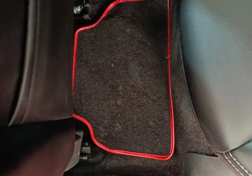 Détail du tapis de sol arrière noir avec bordure rouge dans une Renault Clio Intens rouge, vue intérieure côté gauche.