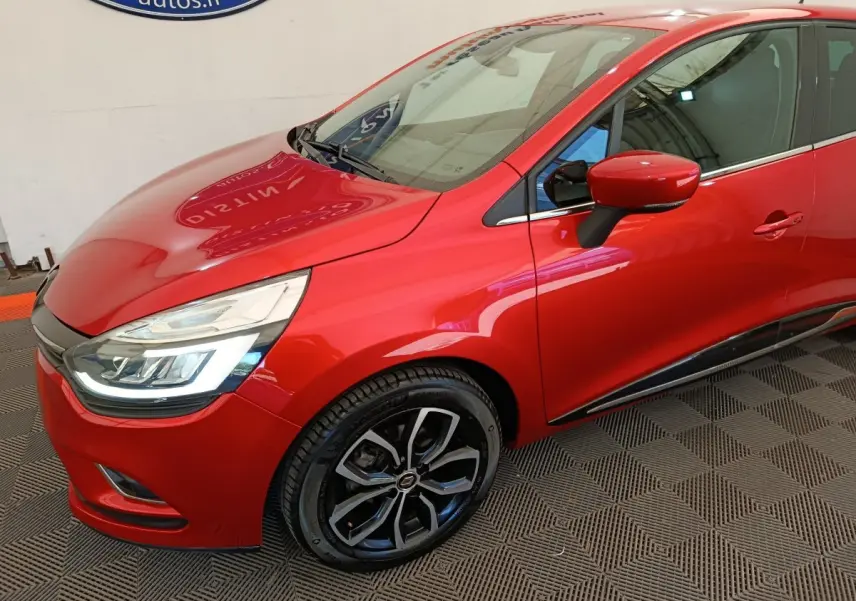 Vue 3/4 avant gauche d'une Renault Clio Intens rouge avec jantes alliage noires et feux LED allumés.
