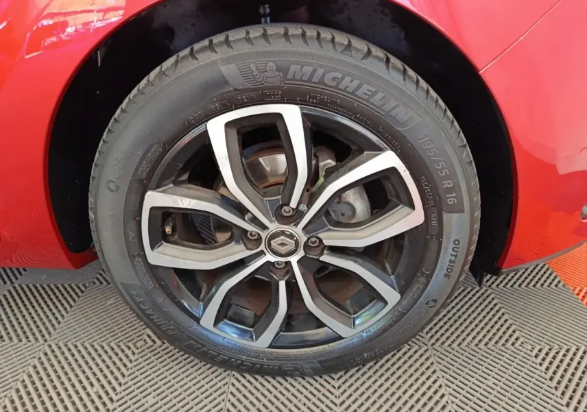 Gros plan sur la roue avant droite d'une Renault Clio rouge, jante alliage noire et argent avec logo Renault central.