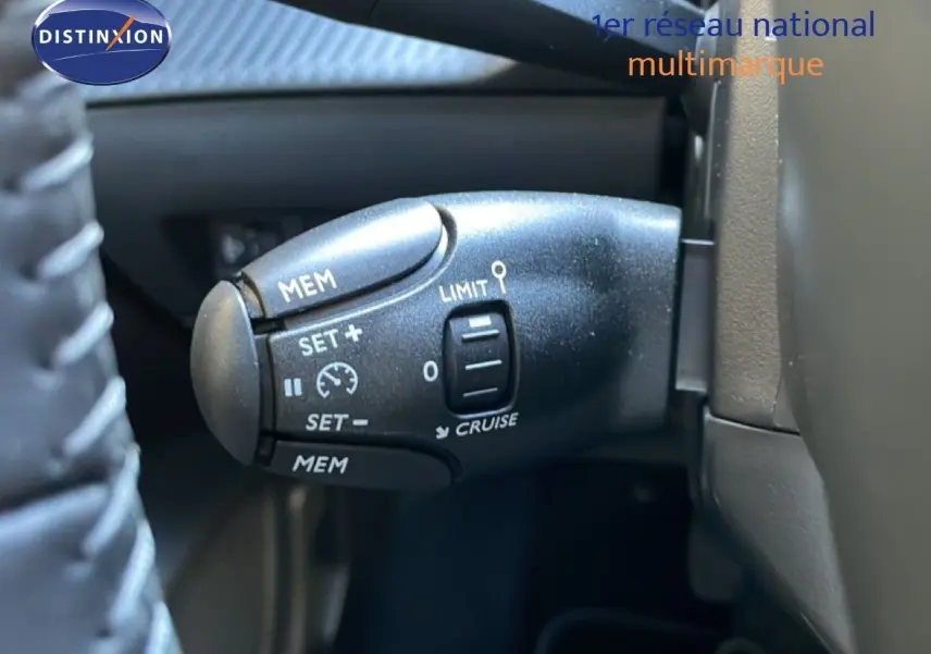 Gros plan sur la commande de régulateur de vitesse au volant d'une Peugeot 208 noire, version hybride 2026.