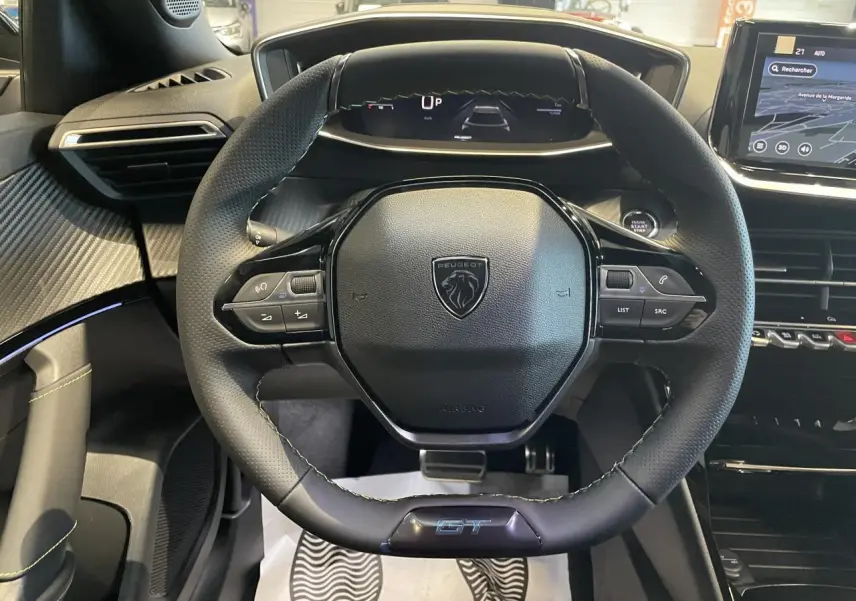 Vue intérieure centrée sur le volant GT noir perforé du Peugeot 2008 1.2i Hybrid avec tableau de bord numérique.