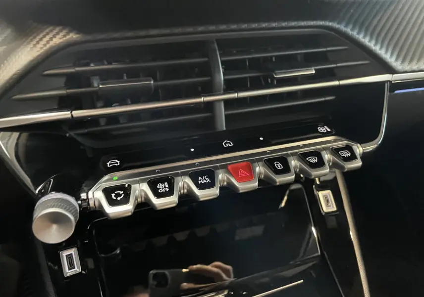 Gros plan sur la console centrale noire brillante du Peugeot 2008 bleu, avec boutons de commande et prises USB visibles.