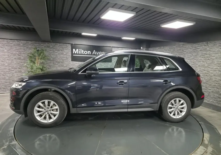 Audi Q5 bleu métallisé vue de profil côté gauche dans un showroom avec jantes 17 pouces et sellerie claire visible.