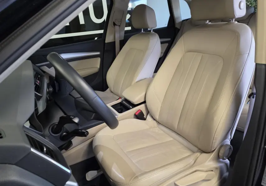 Intérieur Audi Q5 2019 vu côté conducteur, sièges cuir Milano beige avec accoudoir central et volant multifonction.