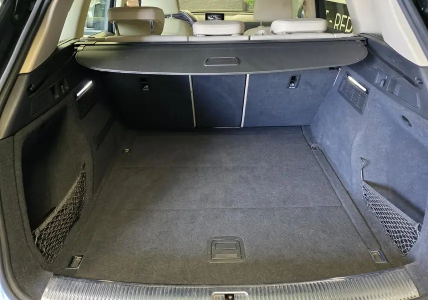 Coffre spacieux de l'Audi Q5 bleu 2019 vu de l'arrière, avec filet de rangement et cache-bagages noir.