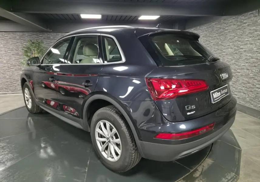 Audi Q5 bleu métallisé vu en 3/4 arrière côté gauche, avec feux arrière LED et jantes en alliage 17 pouces.
