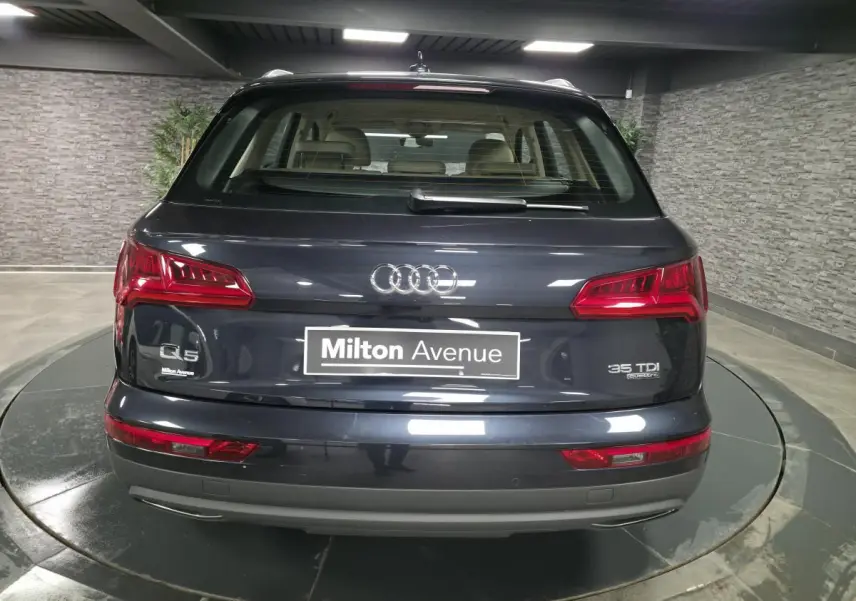 Vue arrière d'un Audi Q5 bleu métallisé avec badges 35 TDI quattro et plaque Milton Avenue dans un garage.