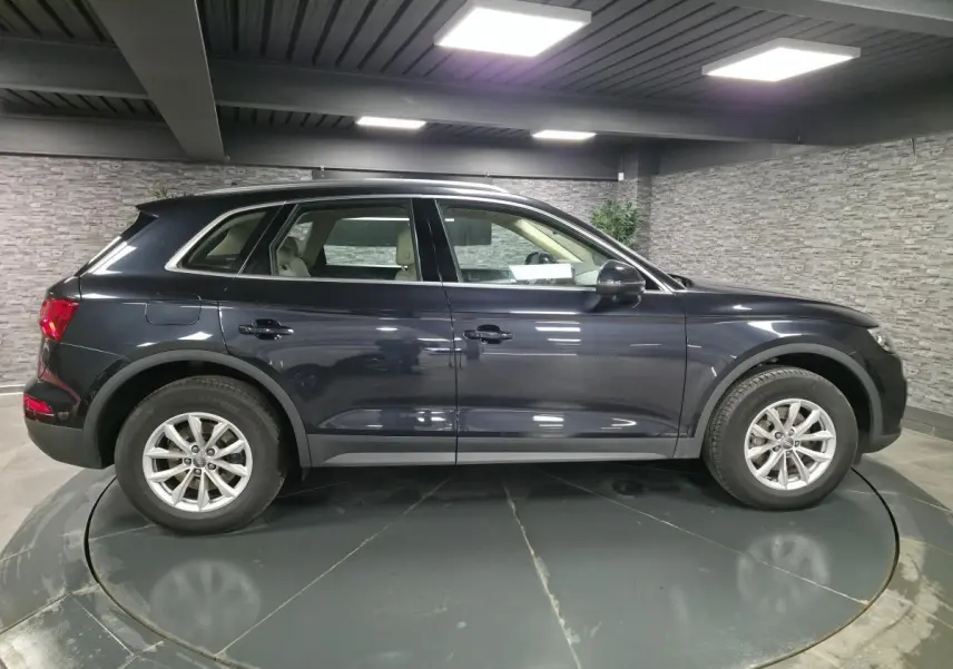 Vue de profil côté gauche d'un Audi Q5 bleu métallisé stationné en intérieur avec jantes aluminium à 10 branches.