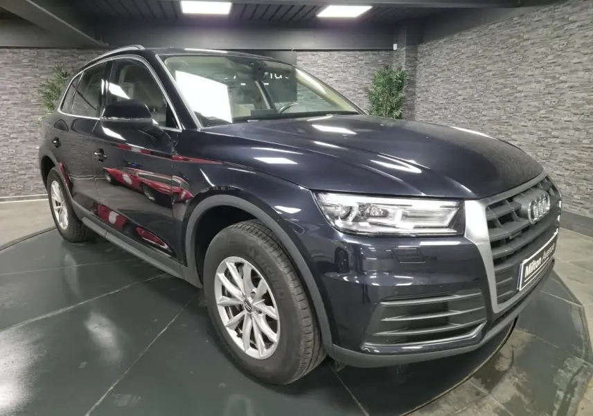 Audi Q5 bleu métallisé en 3/4 avant droit, avec calandre imposante et jantes alliage 17 pouces visibles.