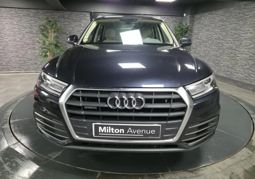 Vue frontale d'un Audi Q5 bleu métallisé avec calandre hexagonale et logo quatre anneaux bien visible.