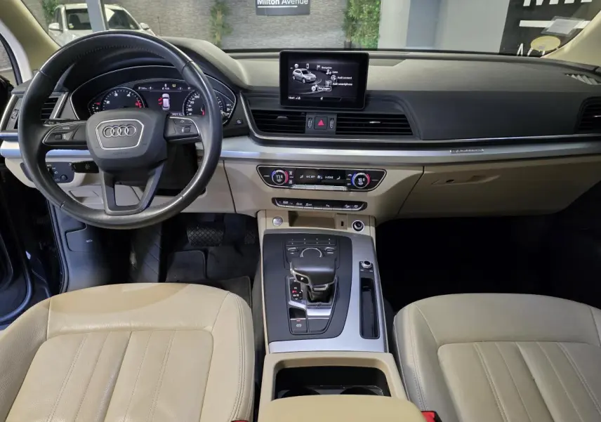 Vue intérieure de l'Audi Q5 2019 montrant le tableau de bord et la sellerie cuir beige avec console centrale moderne.