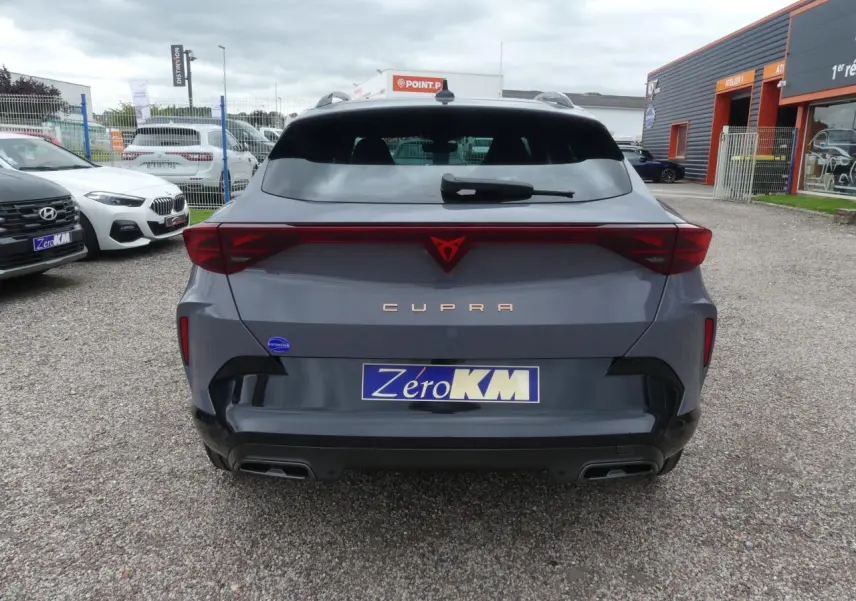 Vue arrière d'une CUPRA Formentor gris Graphène avec logo rouge et double sortie d'échappement noire sur parking.