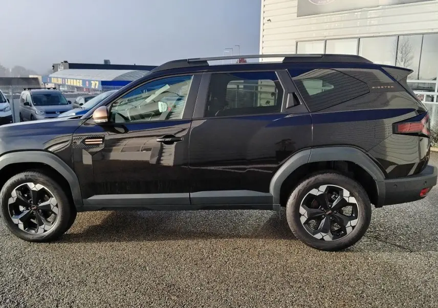 Profil côté gauche du SUV noir Dacia Bigster 2025 avec jantes bi-ton et toit surélevé, stationné en extérieur.