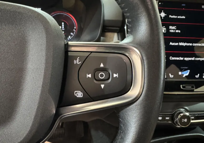 Gros plan sur les commandes au volant côté gauche du Volvo XC40 Recharge T5 noir, avec écran tactile en arrière-plan.
