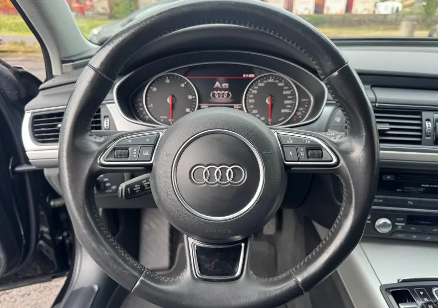 Vue centrée sur le volant en cuir noir de l'Audi A6 Avant 2015 avec tableau de bord et commandes visibles.
