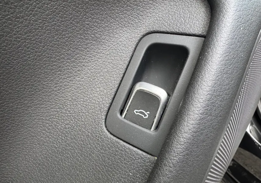 Gros plan sur le bouton d'ouverture du hayon dans l'habitacle noir de l'Audi A6 Avant 2015.