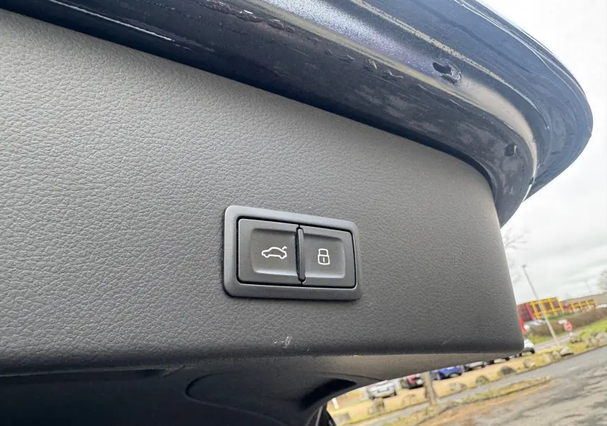 Gros plan sur les boutons d'ouverture et de verrouillage du hayon du coffre d'une Audi A6 Avant noire, vue depuis l'arrière.