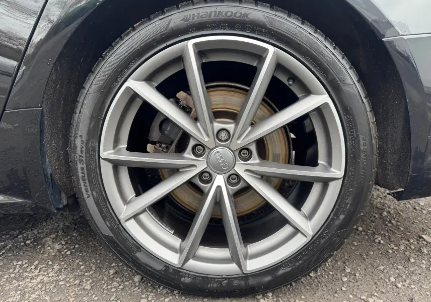 Gros plan sur la roue avant droite d'une Audi A6 Avant noire de 2015, jante alliage 19 pouces avec logo Audi au centre.