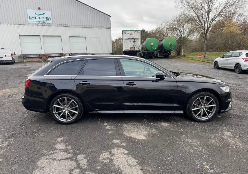 Audi A6 Avant noire vue de profil côté gauche, avec jantes alliage et vitres teintées sur parking extérieur.