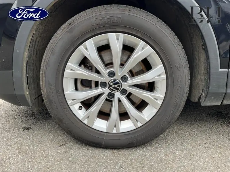 Gros plan sur la jante alu argentée avec logo VW d’un Volkswagen Tiguan noir intense nacré, côté droit.