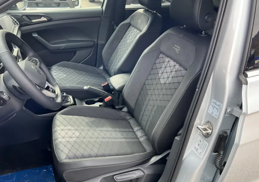 Vue intérieure côté conducteur du Volkswagen T-cross gris argent 2025, sièges tissu avec surpiqûres et logo R brodé.