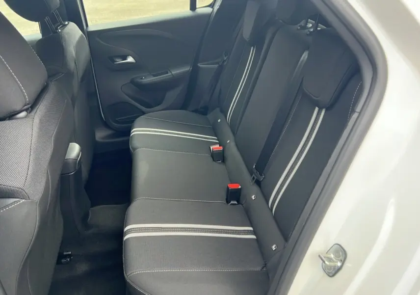 Vue intérieure arrière côté droit de l’Opel Corsa blanc kontur, banquette noire avec bandes grises et ceintures de sécurité.