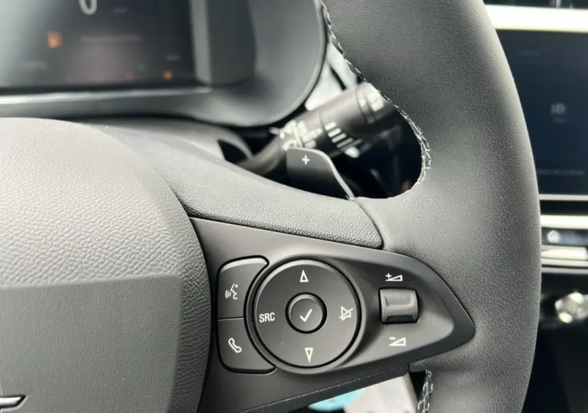 Gros plan sur les commandes multifonctions noires du volant cuir d’une Opel Corsa blanc kontur, version hybride 2026.
