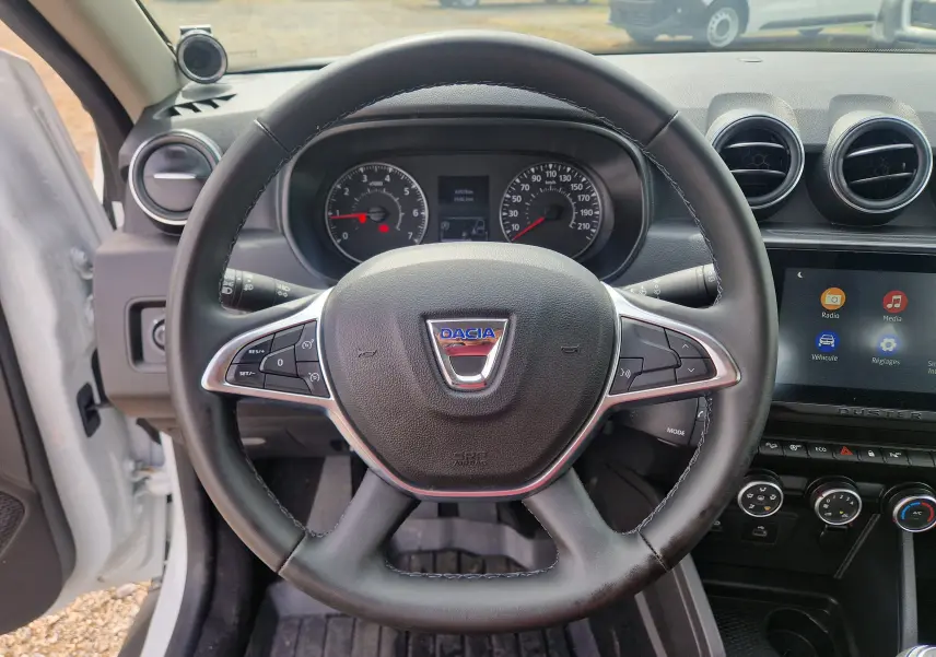 Vue intérieure centrée sur le volant du Dacia Duster blanc 2022, avec tableau de bord et écran tactile visibles.