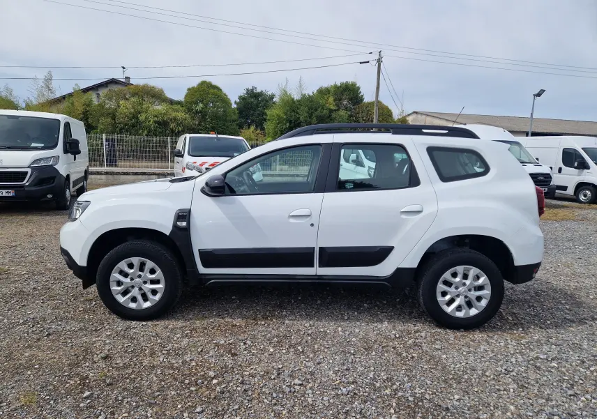 Profil côté gauche d'un Dacia Duster blanc 4x4 2022 avec protections noires et jantes alliage 16 pouces.
