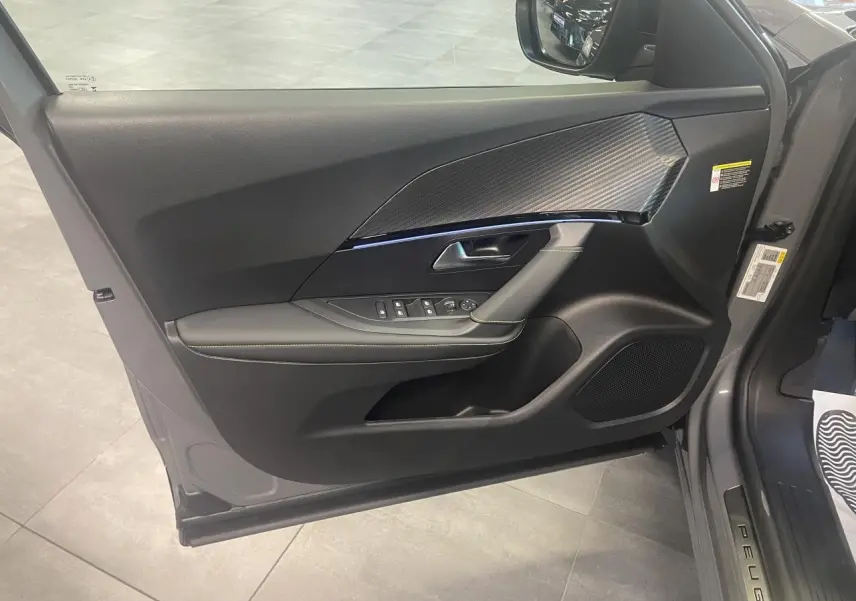Vue intérieure de la porte avant gauche gris métallisé du Peugeot 2008 1.2i Hybrid GT avec insert carbone et commandes électriques.