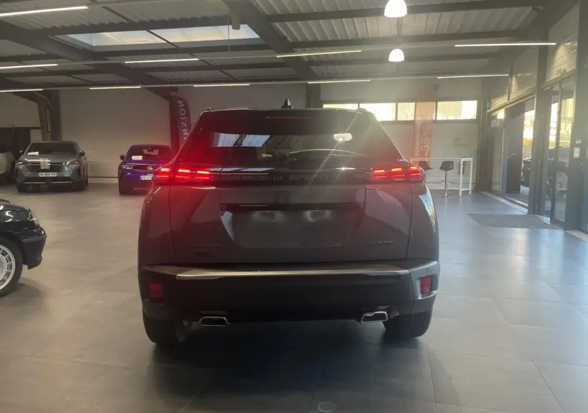 Vue arrière d'un Peugeot 2008 gris métallisé avec feux arrière LED allumés dans un showroom.
