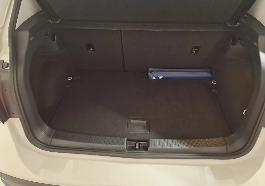 Coffre ouvert du Volkswagen T-Cross 2024 gris Ascot, vue plongeante montrant un espace de rangement vide avec un kit bleu.