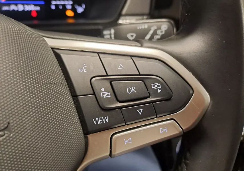 Gros plan sur les commandes au volant du Volkswagen T-Cross 2024, boutons noirs avec cadre argenté.