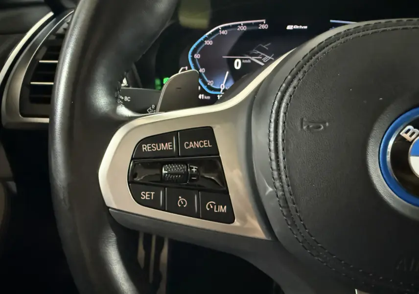 Gros plan sur le côté gauche du volant cuir noir d'une BMW X3 bleu 2023 avec commandes de régulateur de vitesse et tableau de bord digital.