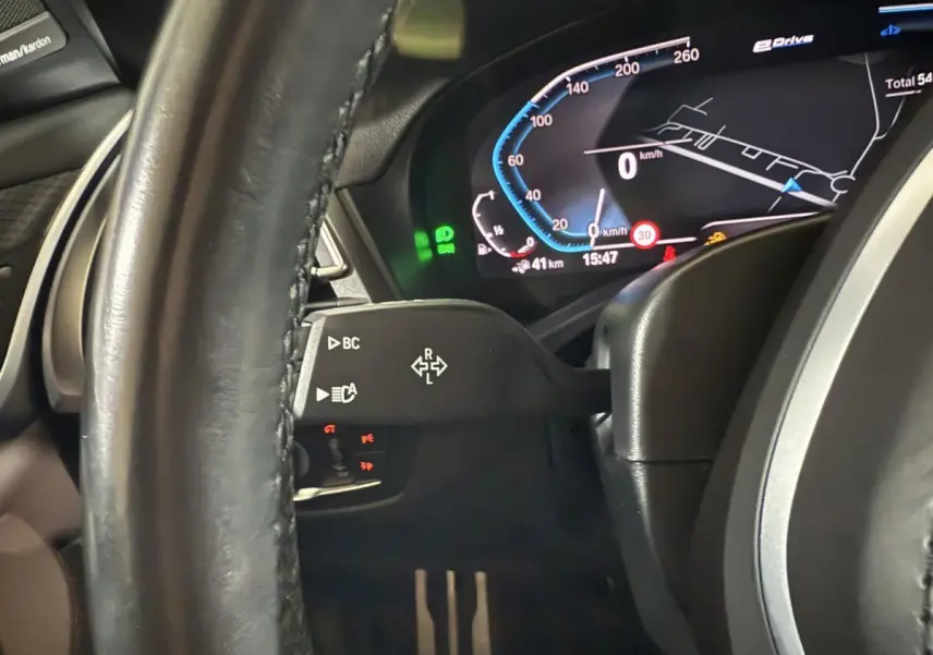 Gros plan sur le tableau de bord numérique et le volant cuir noir du BMW X3 xDrive30e 2023, affichage vitesse et navigation.