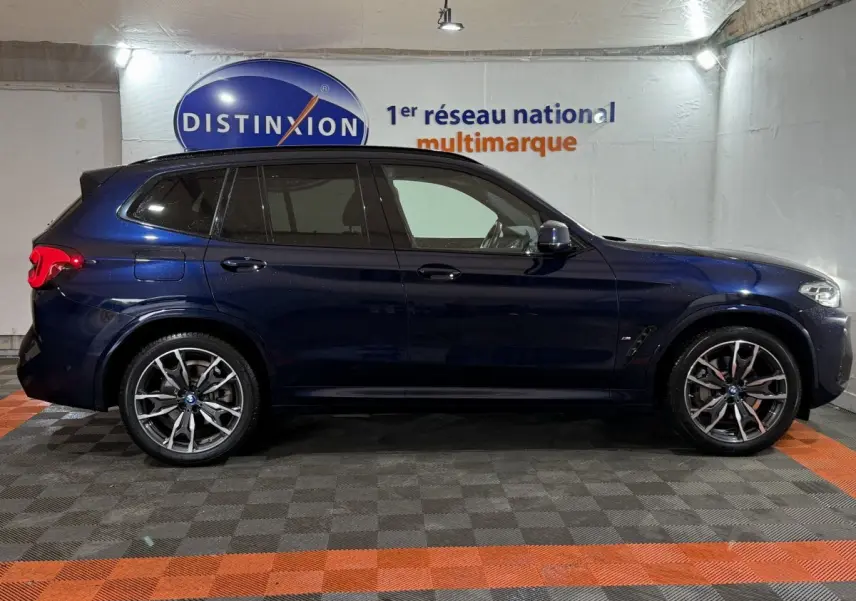 Profil côté gauche d'un BMW X3 xDrive30e bleu 2023 avec jantes alliage et vitres teintées en intérieur showroom.