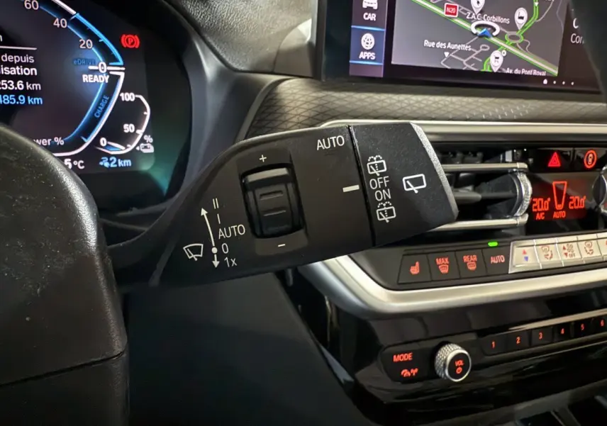 Gros plan sur la commande d'essuie-glace et le tableau de bord numérique d'une BMW X3 xDrive30e bleu 2023, affichage tactile visible.
