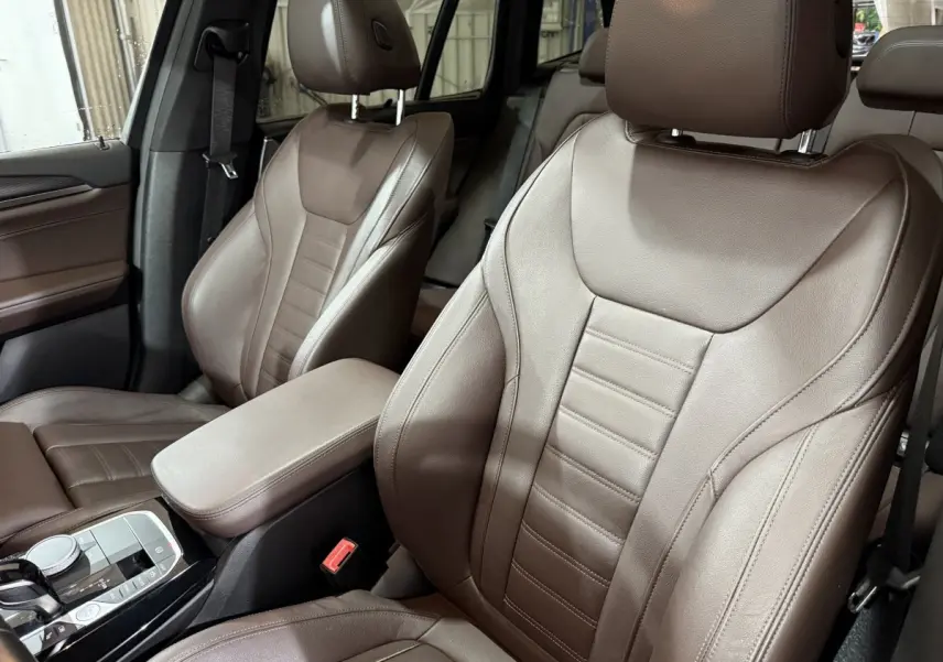 Gros plan sur les sièges avant en cuir marron du BMW X3 xDrive30e 2023, avec console centrale et molette de sélection visibles.