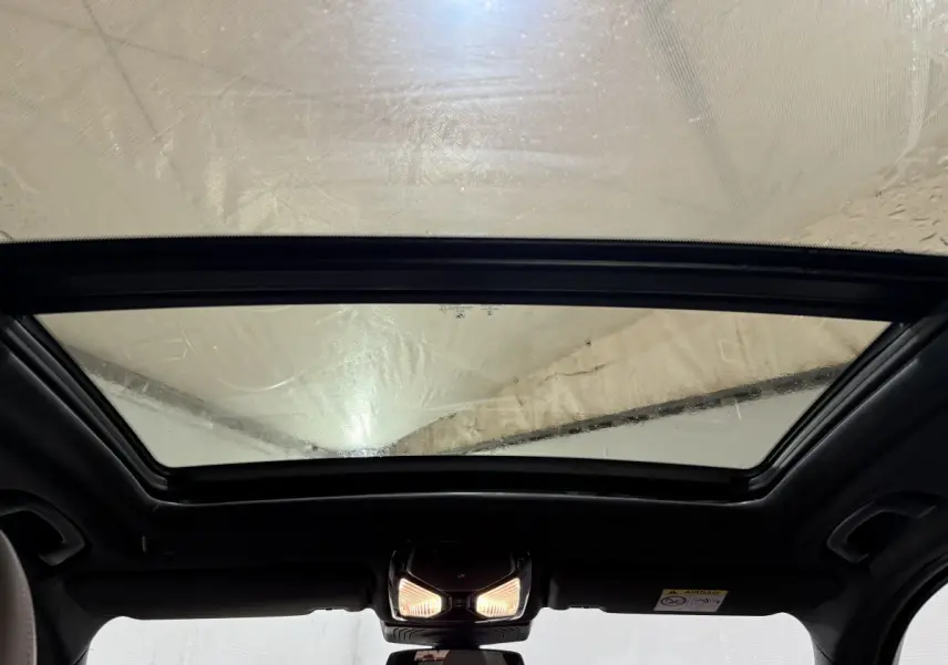 Toit panoramique en verre vu de l'intérieur d'un BMW X3 bleu, éclairage intérieur allumé au centre du plafond.