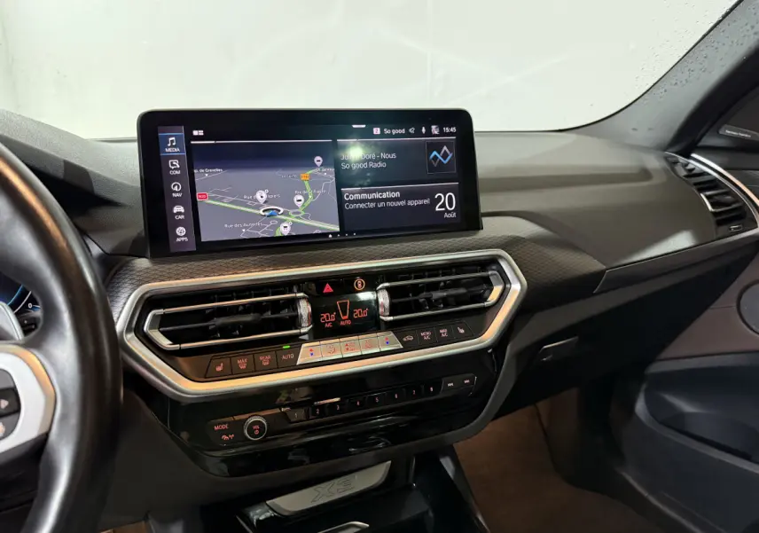 Vue intérieure du tableau de bord du BMW X3 xDrive30e 2023 avec écran tactile 12,3 pouces et commandes climatisation digitales.
