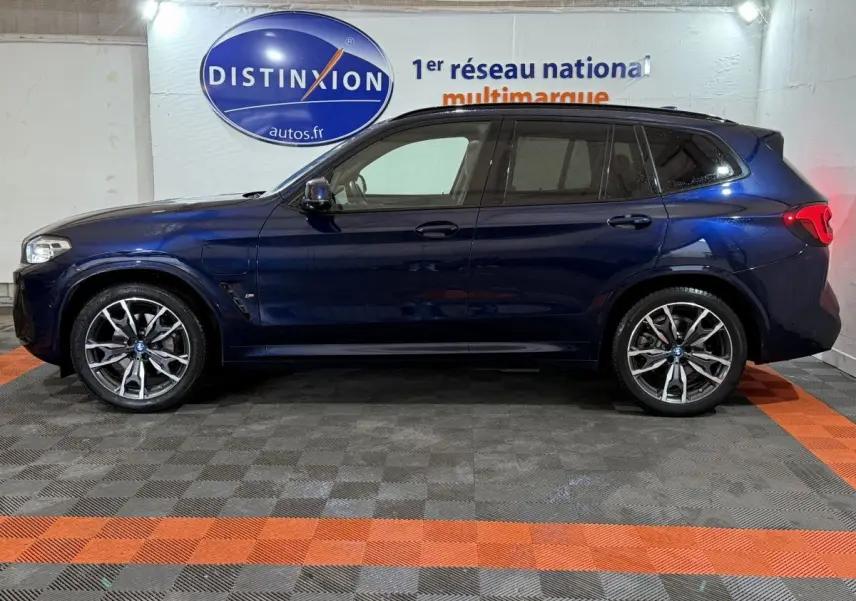 Profil côté gauche d'un BMW X3 xDrive30e bleu 2023 M Sport avec jantes alliage et vitres teintées en intérieur showroom.
