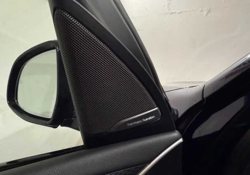 Gros plan sur l'enceinte Harman/Kardon et le rétroviseur côté conducteur d'un BMW X3 bleu 2023.