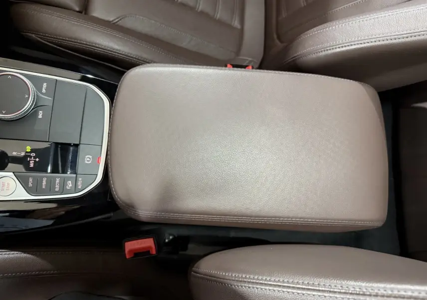 Vue plongeante sur l'accoudoir central en cuir marron et la console de commande du BMW X3 xDrive30e 2023 M Sport.