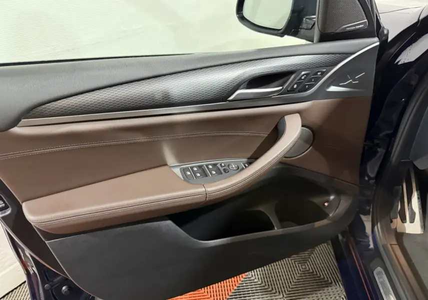 Vue côté gauche de la porte avant d'une BMW X3 bleu, garniture marron avec commandes électriques et logo M Sport.