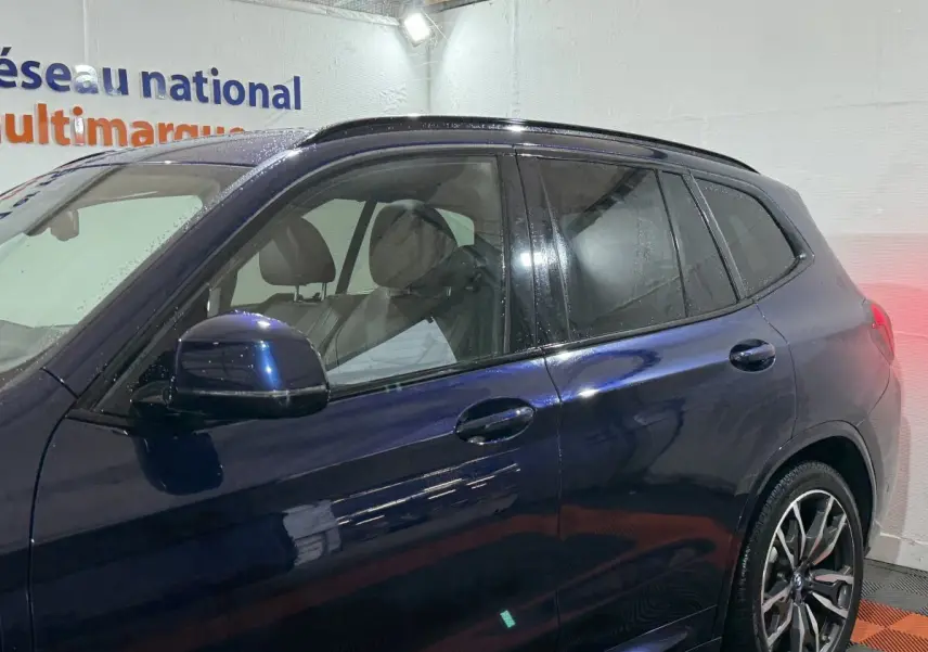 BMW X3 xDrive30e bleu vu de profil côté gauche, avec jantes alliage et vitres teintées dans un garage.